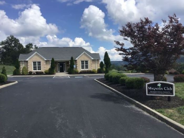 The Magnolia Club clubhouse building with its sign and mountain backdrop